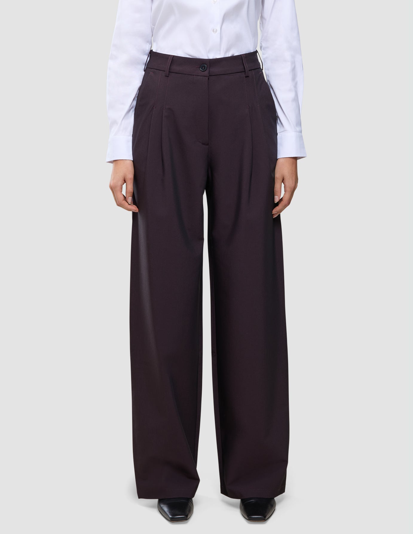 En person bär en vit skjorta med knappar och dambyxorna Avira Pants Wide i färgen Burgundy Berry, som har en avslappnad passform med vida ben.